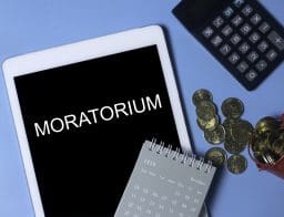 Táblagép "MORATORIUM" felirattal, számológép, pénzérmék és naptár a képen.