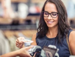 Bankkártyás fizetést végez egy szemüveges nő egy boltban.