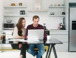 Fiatal pár otthonról a laptop előtt intézi pénzügyeit - online lakáshitelt is lehet igényelni.