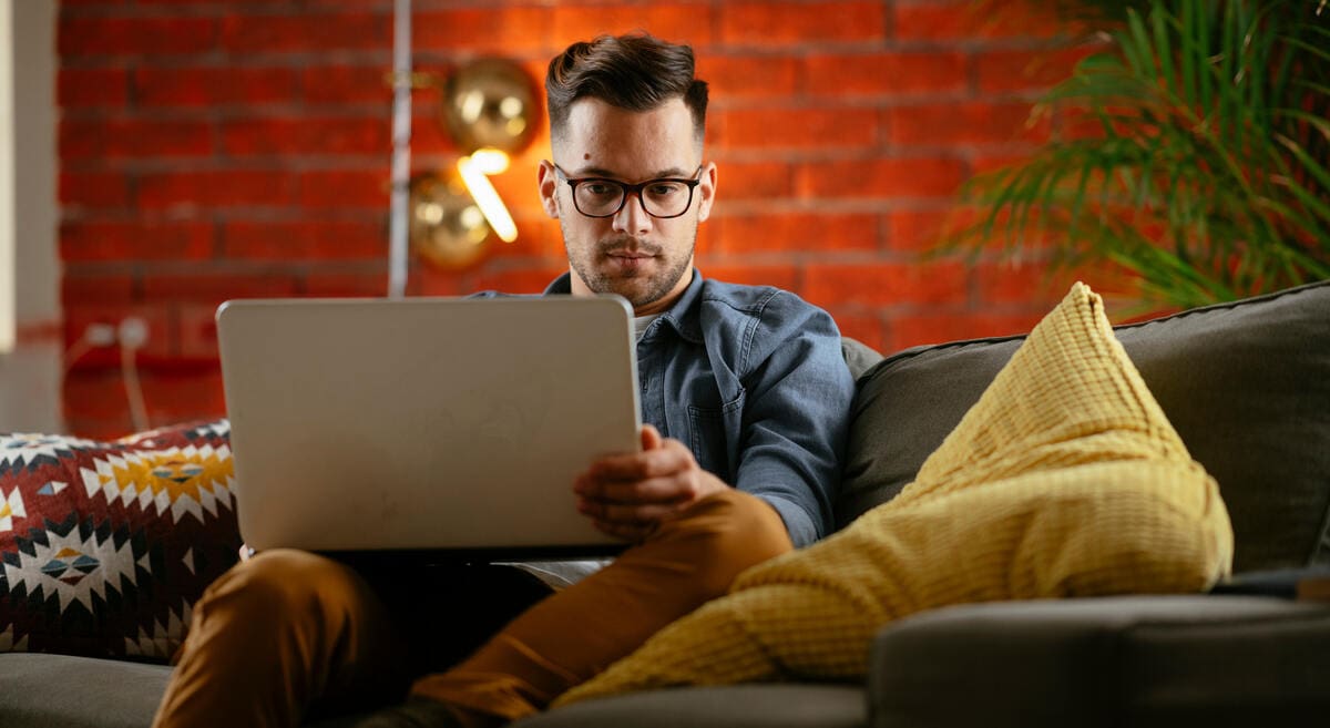 férfi a kanapén Prémium Euró Magyar Állampapírt vásárol a laptopján