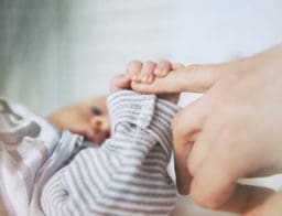 Egy kis csecsemő megfogja az anyukája feléje nyújtott ujját.