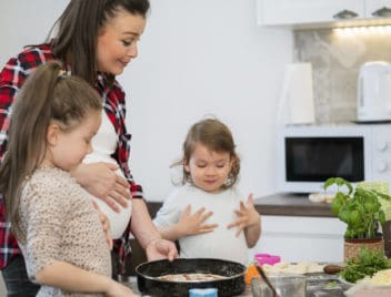 Várandós anyuka két kislányával pizzát sütnek.