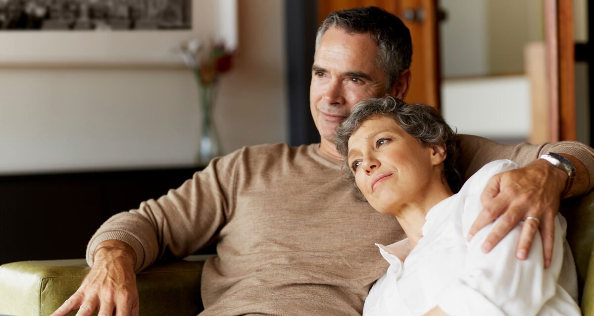 középkorú pár a kanapén ülve, nappaliban azon tanakodik, mekkora havi nyugdíj-megtakarítás szükséges