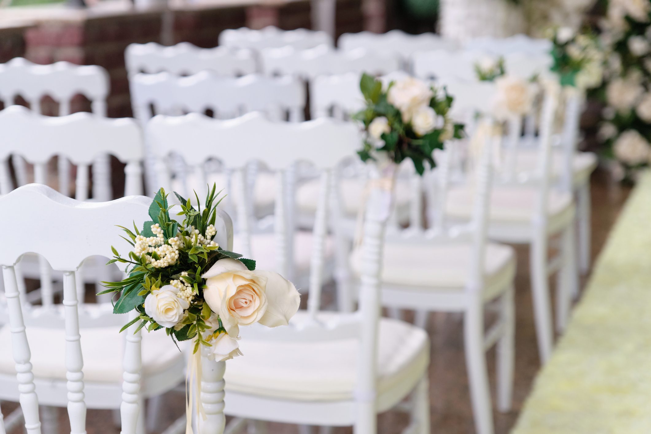 Fehér széksorok esküvői dekorral a házasságkötési ceremóniára, hátulról fényképezve.
