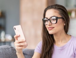 Egy fiatal, szemüveges, hosszú, barna hajú nő nézi a telefonját, személyi kölcsön kedvezményeket?