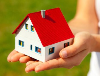 zöld mezőn nő kezében miniatűr házikó, lakástakarékot vesz fel lakáshitel mellé, teljes visszafizetendő összeg csökken