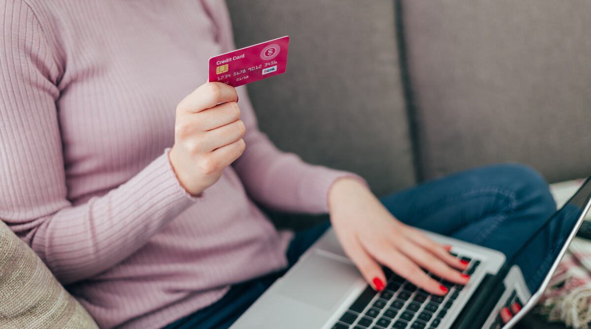 nő kezében bankkártya, ölében laptop, online vásárlás közben, bankszámla megszüntetése előtt