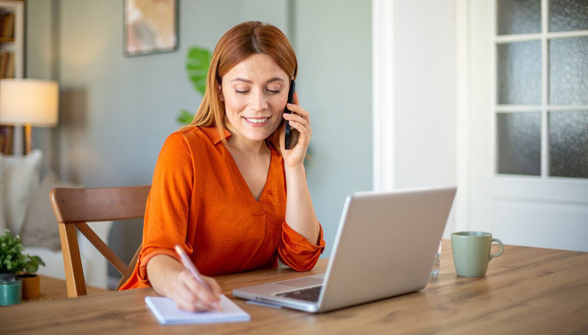 fiatal nő laptop előtt telefonál, számlaváltást intéz bankon belül telebankon