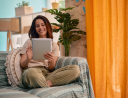 Egy fiatal nő otthona kényelméből végzi az ügyintézést egy tablettel a kazében.