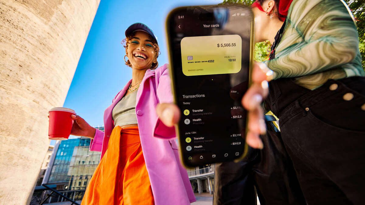 gen z nő a mobilbankok funkcióit mutatja az utcán, kávéval a kezében