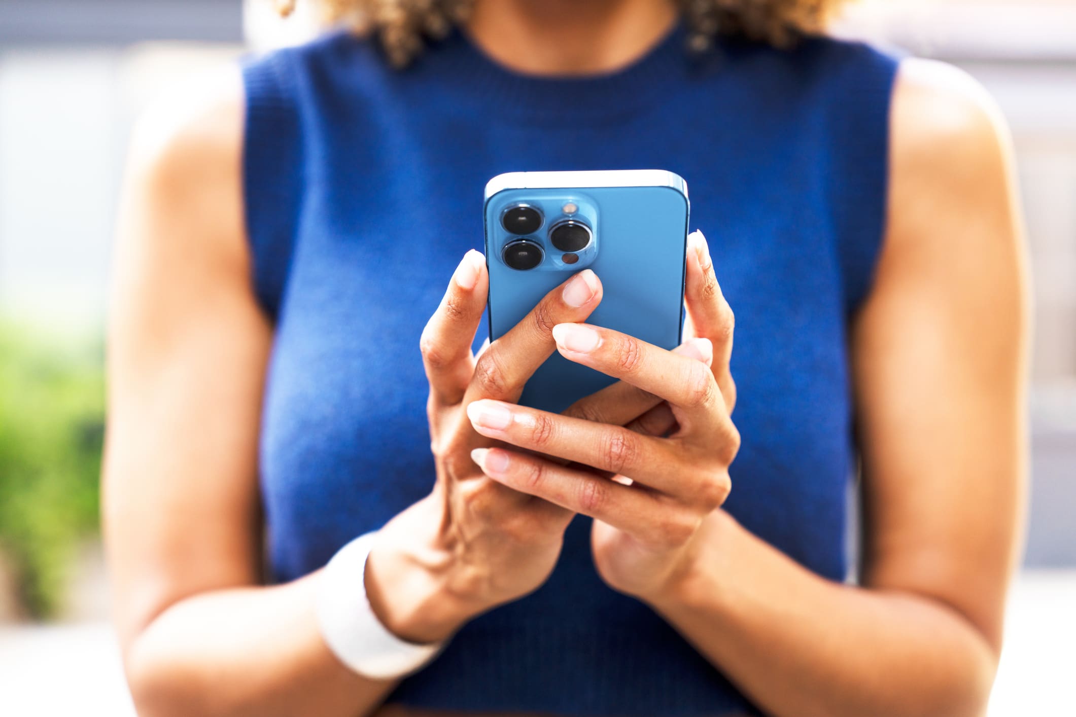 Egy kék ruhába öltözött női alak mobiltelefont nyomkod.