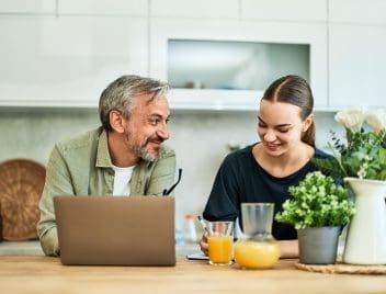 Egy férfi és a lánya ülenk a konyhában, előttük egy laptop, a lény jegyzetel, előttük narancslé.