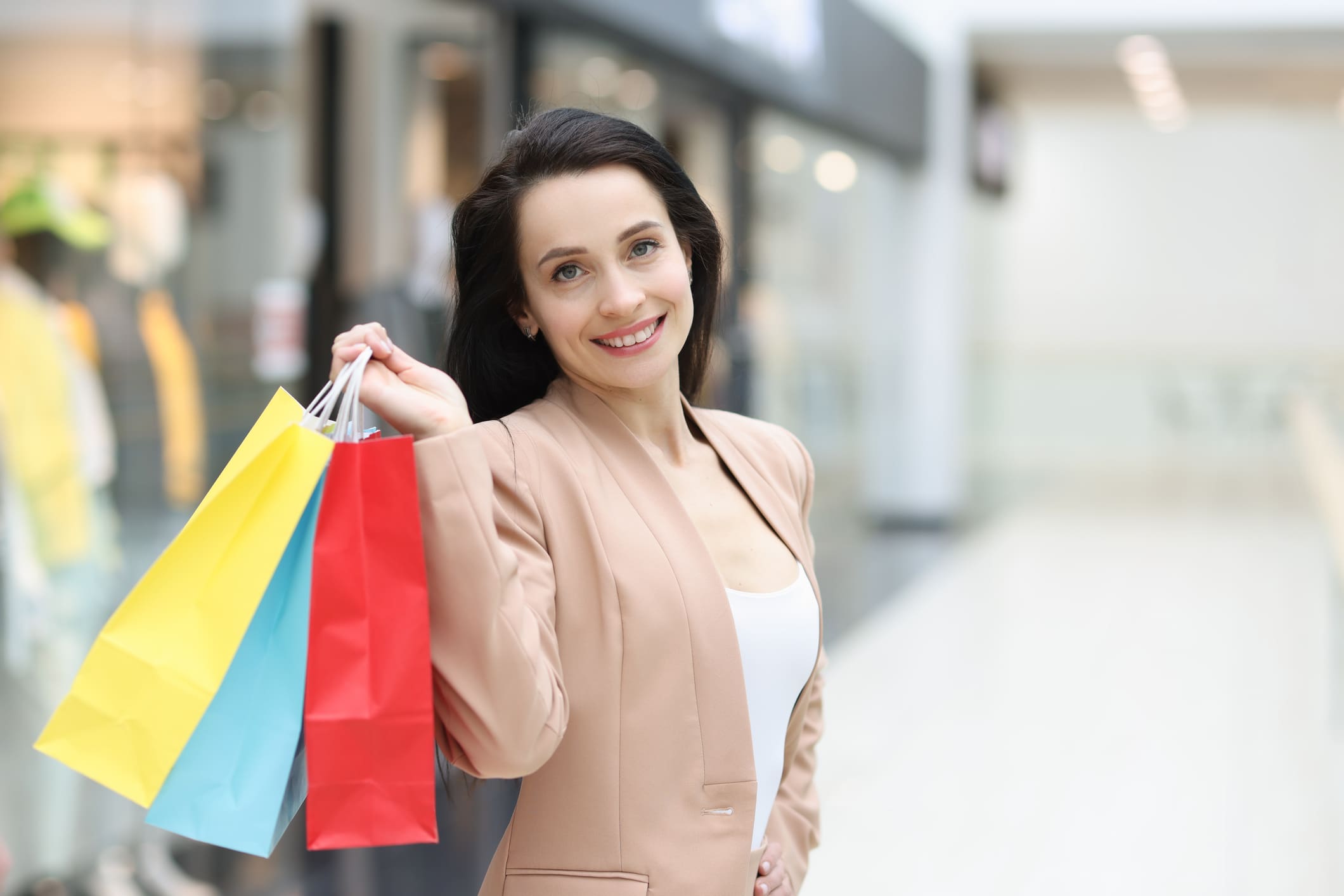 Fiatal csinos nő shoppingol, már van a vállán egy sárga, egy kék és egy piros papírszatyor