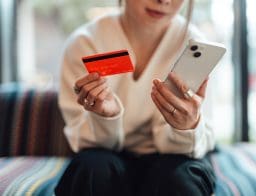 Egy női sziluett látszik, egyik kezében mobiltelefon, másikban bankkártya.