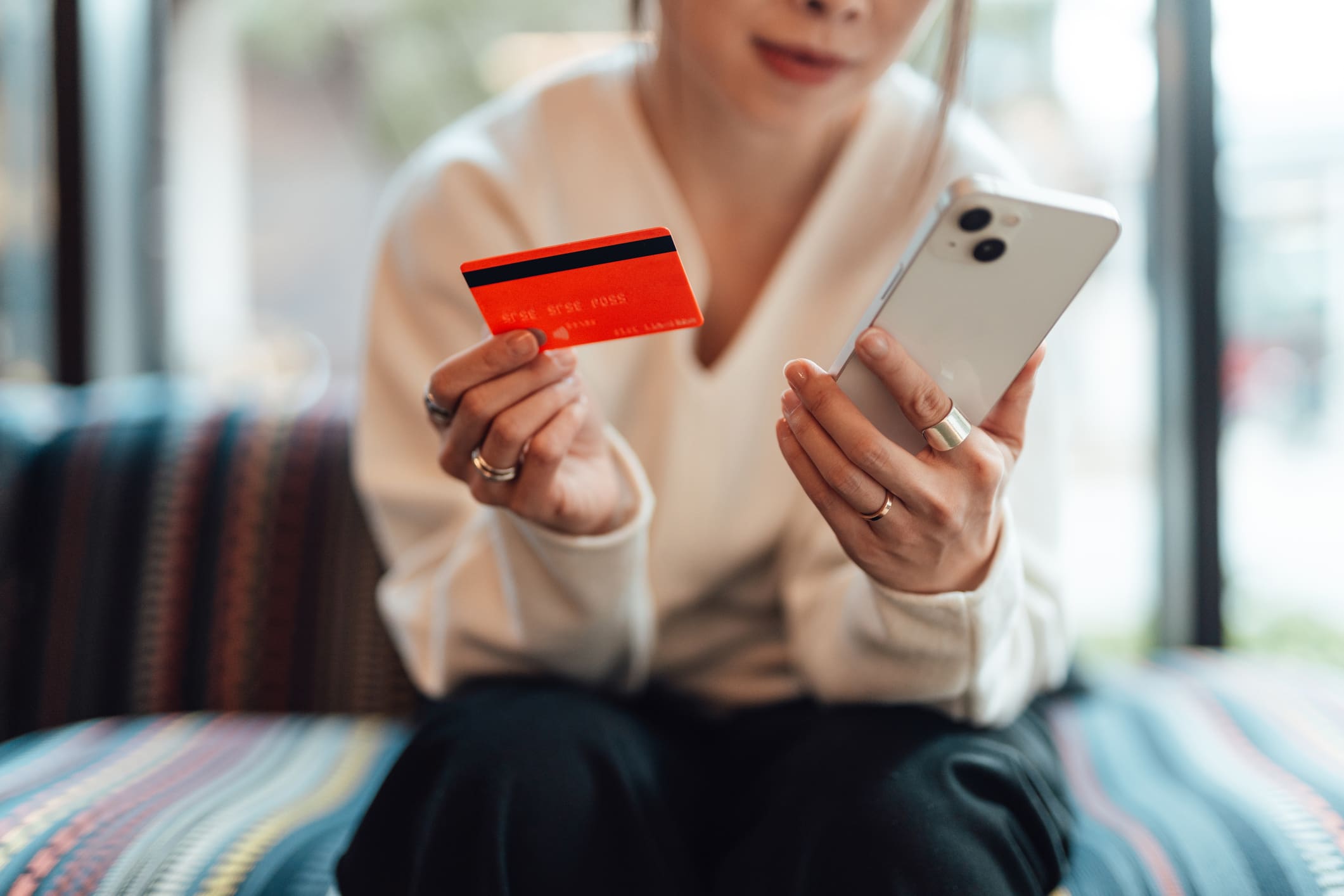 Egy női sziluett látszik, egyik kezében mobiltelefon, másikban bankkártya.