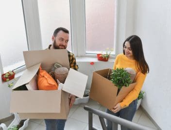 Egy nő és egy férfi költözködik: visznek fel az emeletre egy-egy kartondoboz holmit.