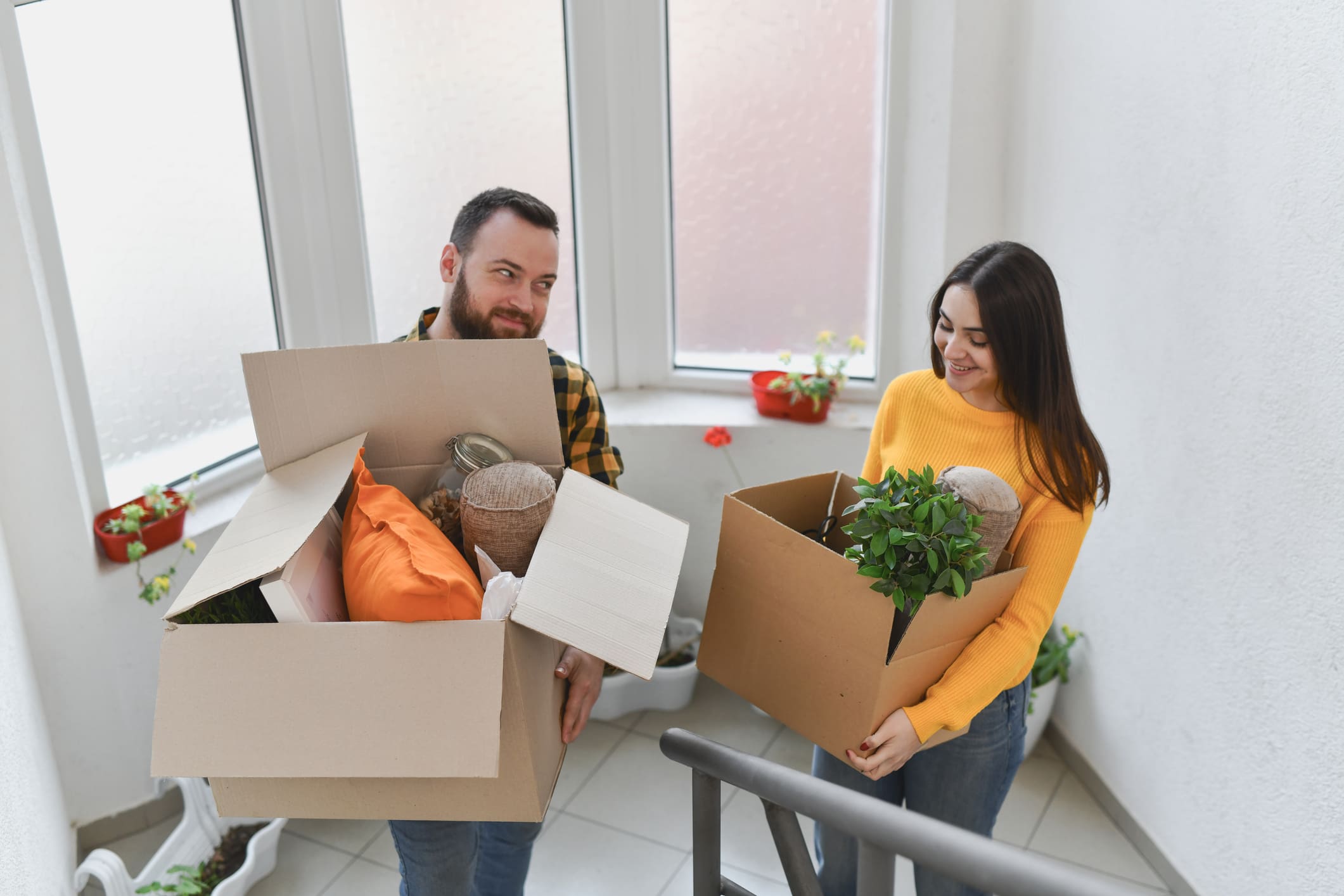 Egy nő és egy férfi költözködik: visznek fel az emeletre egy-egy kartondoboz holmit.