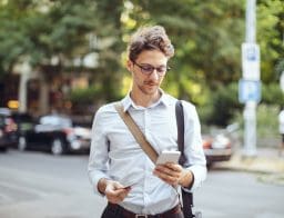 Egy inges, fiatal férfi a város utcáin kezében mobiltelefonnal és bankkártyával.