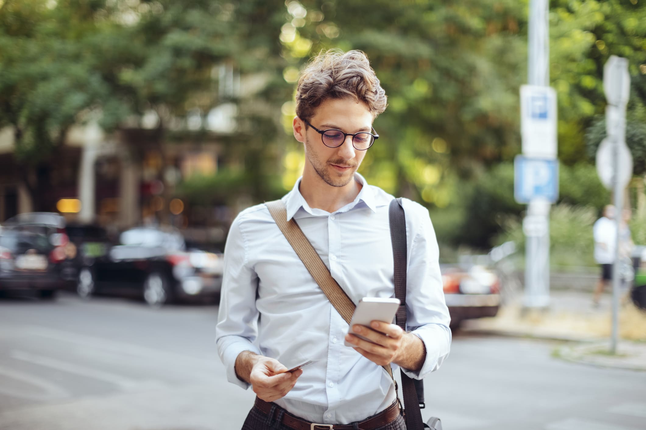 Egy inges, fiatal férfi a város utcáin kezében mobiltelefonnal és bankkártyával.