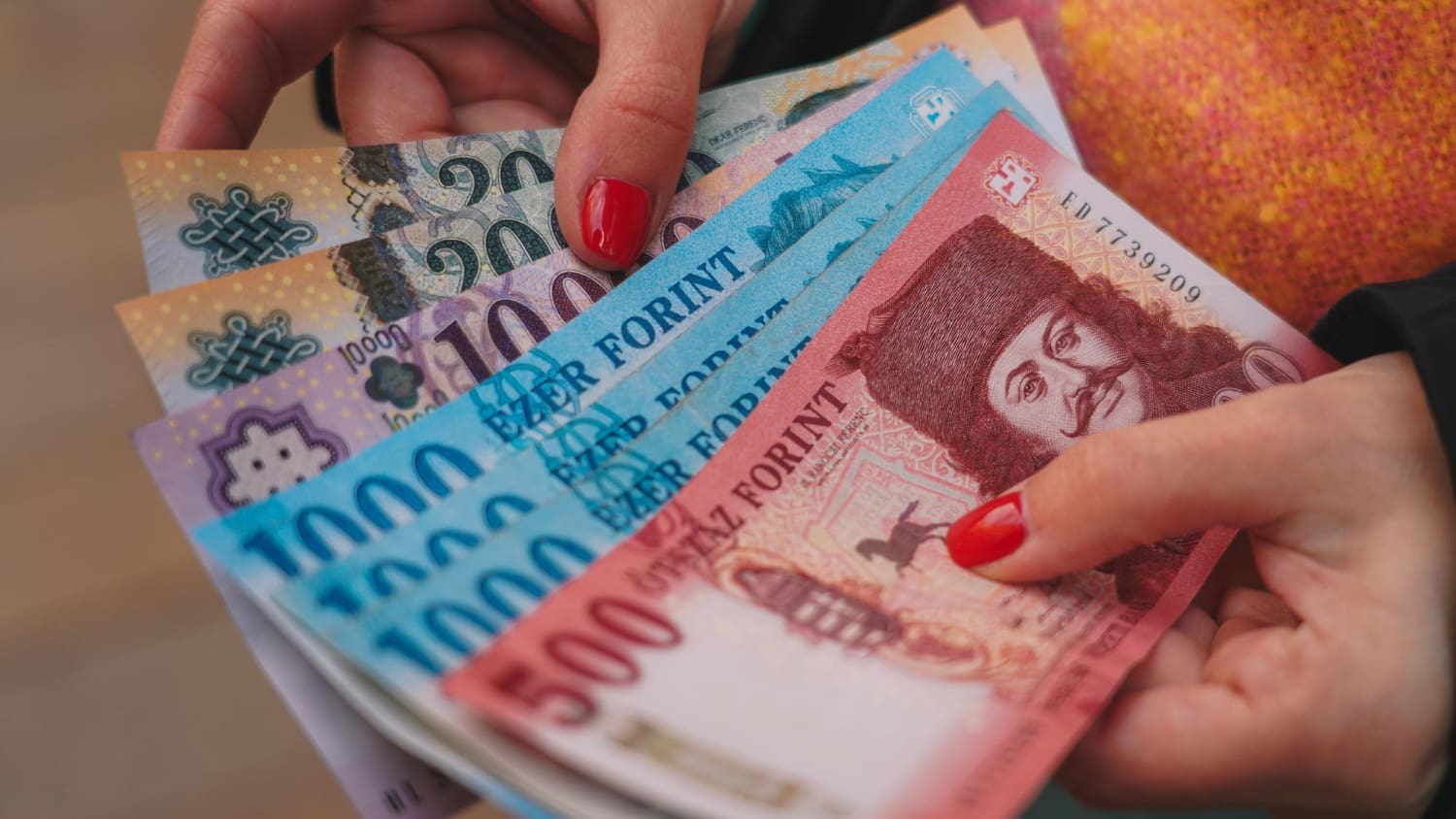 Magyar forint bankjegyek egy piros körömlakkos nő kezében.