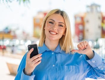 Fiatal, szemüveges lány örül a mobiltelefonjára kapott hírnek.