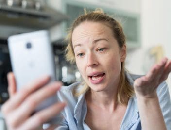 Egy fial nő nézi a mobiltelefonját és értetlen arcot vág.
