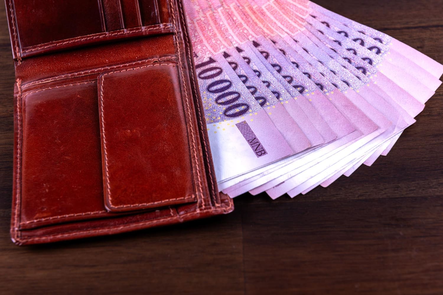 Magyar 10 ezer forintos köteg lóg ki egy barna bőr nyitott pénztárcából.
