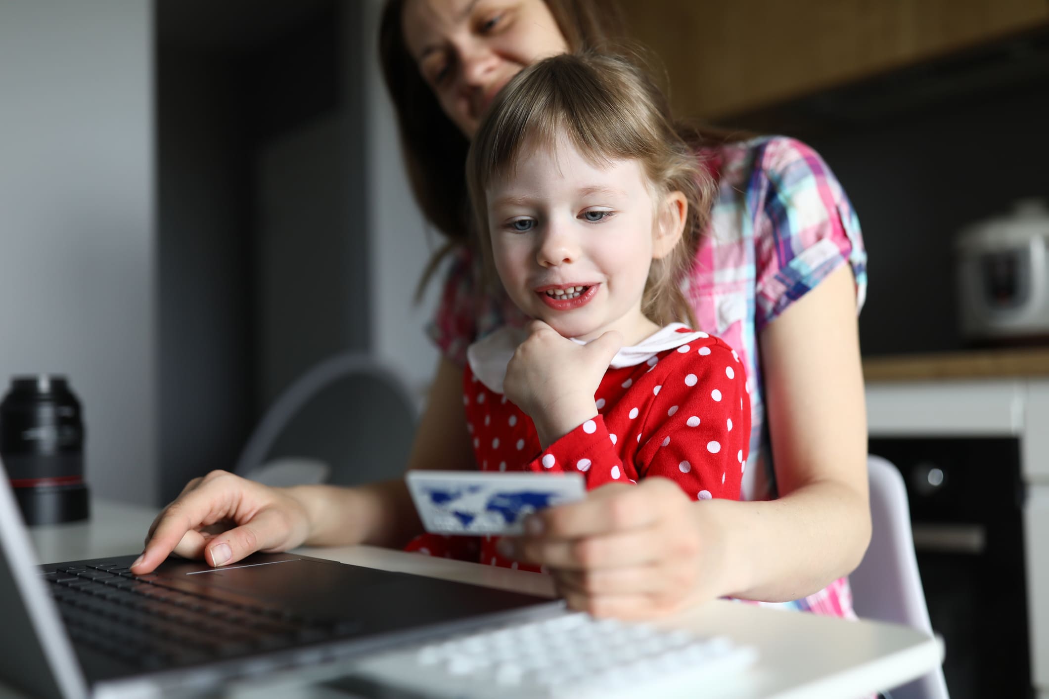 Egy fiatal anyuka ül egy laptop előtt, ölében a kislányával, kezében egy brosúrával.