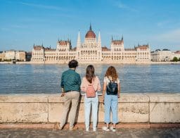Egy férfi és két nő a budai oldalról nézi a Duna másik oldalán lévő Parlament épületét Budapesten.