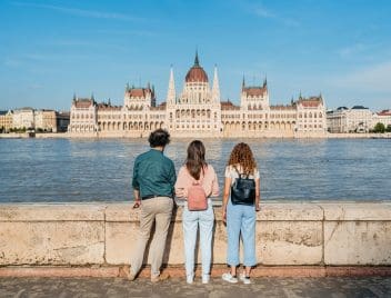 Egy férfi és két nő a budai oldalról nézi a Duna másik oldalán lévő Parlament épületét Budapesten.