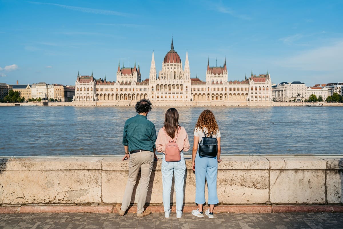 Egy férfi és két nő a budai oldalról nézi a Duna másik oldalán lévő Parlament épületét Budapesten.