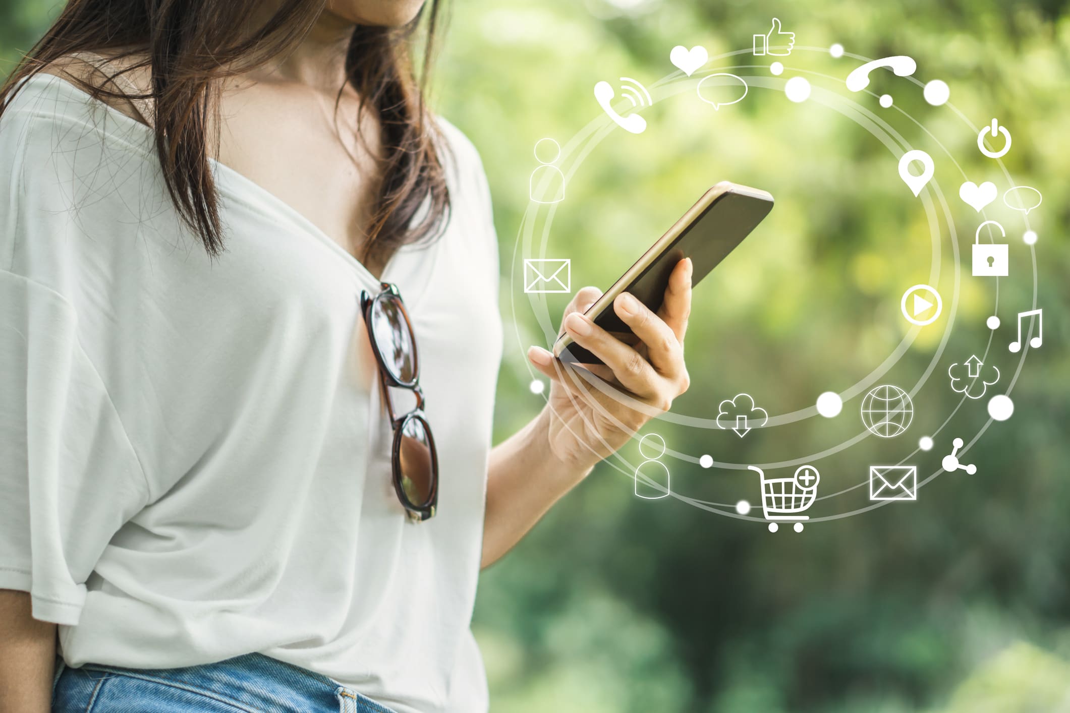 Egy nő kezében látunk egy mobiltelefont, fás háttérrel. A mobultelefon körül egy körívben kis ikonok, amik bármely bankolási tevékenységre utalhatnak.