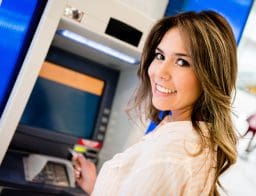 Egy fiatal csinos nő áll az ATM előtt, de a kamerába néz