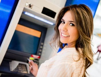 Egy fiatal csinos nő áll az ATM előtt, de a kamerába néz